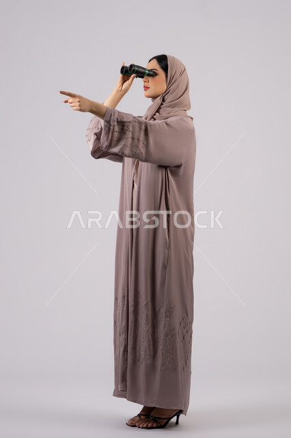 ايماءات الدهشه و الاستغراب, الاشارة الي شئ ما، التخطيط المستقبلي للأهداف و الطموحات، شابة سعودية تقوم برؤية الاشياء البعيدة عبر التلسكوب، بورتريه من الجانب لامرأة عربية خليجية اماراتية محجبة ترتدي العباءة والحجاب تنظر من خلال منظار ،حب الاستكشاف والمغامرة