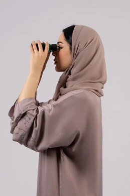 شابة سعودية تقوم برؤية الاشياء البعيدة عبر التلسكوب، محاولة رؤيه شئ ما، بورتريه من الجانب لامرأة عربية خليجية اماراتية محجبة ترتدي العباءة والحجاب تنظر من خلال منظار بايماءات الدهشه و الاستغراب, حب الاستكشاف والمغامرة،التخطيط المستقبلي للأهداف و الطموحات