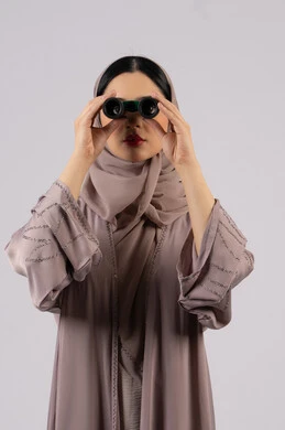 بورتريه لامرأة عربية خليجية اماراتية محجبة ترتدي العباءة والحجاب تنظر من خلال منظار بايماءات الدهشه و الاستغراب, حب الاستكشاف والمغامرة،التخطيط المستقبلي للأهداف و الطموحات، شابة سعودية تقوم برؤية الاشياء البعيدة عبر التلسكوب