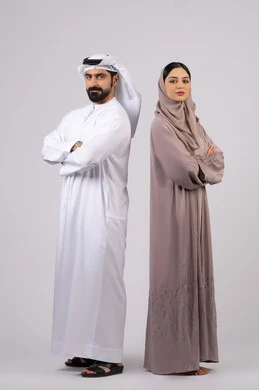 Standing with crossed hands and self-confidence, expressions of seriousness and focus, portrait of an Arab Gulf Emirati couple wearing Emirati dress looking at something, concept of elegance and interest in outward appearance, full body length, white background