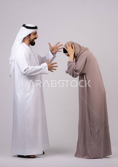 رجل اماراتي يضرب زوجته بعنف ، شجار بين الزوجين ، سوء تفاهم ، مشاكل عائلية وصراع اسري ،بورتريه لزوجان عربيان خليجيان اماراتيان يتجادلان مع بعض،  ازمة في العلاقات الاسرية ، خلفية بيضاء
