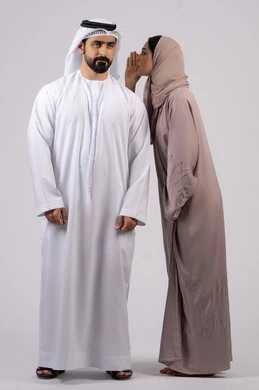 ايماءات الانصات والتركيز بالكلام ، النميمة والتحدث عن شخص ما ، التحدث بصوت منخفض ، بوررية لامراه عربية خليجية اماراتية ترتدي العباءة والحجاب تهمس باذن زوجها ، مفهوم الكتمان وحفظ الاسرار بين الازواج،خلفية بضاء