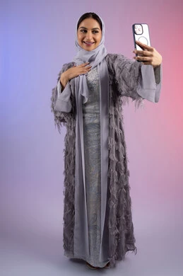 Communicating and talking with family and friends, a Saudi woman taking selfies, making a video call via mobile phone, portrait of an Arab Gulf Emirati woman wearing a colorful abaya holding a mobile phone in her hand, full body, colorful background