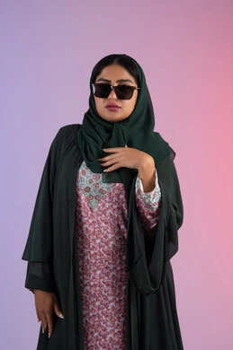 Beauty and appearance care, interest in fashion and elegance, portrait of an Arab Gulf Emirati woman wearing a colorful abaya and sunglasses, looking with confidence and self-esteem, a young Saudi woman looking at the camera with gestures of coquettishness and femininity, colorful background