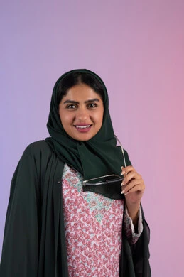 عرض الأزياء والموديلات الحديثة، الاهتمام بالموضة والأناقة, بورترية لامراة عربية خليجية إماراتية ترتدي العباءة الملونه تمسك بيدها النظارة الشمسية  , شابة سعودية تقف بإيماءات الدلع و الانوثه, خلفية ملونه