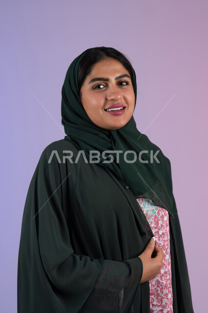 الاهتمام بالأناقة والمظهر الخارجي، مفهوم العناية بالجمال والإطلالة المتميزة، بورترية مقرب لسيدة عربية خليجية اماراتية مبتسمه محجبة ترتدي العباءه الملونه ، سيدة سعودية تنظر الى الكاميرا بايماءات السعادة و السرور، خلفية ملونه