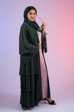 Fashion models for veiled women, softness, elegance and femininity, the concept of beauty care and a distinguished look, a side portrait of a smiling veiled Emirati Gulf Arab woman wearing a colorful abaya holding sunglasses in her hand, a Saudi woman looking at the camera with gestures of happiness and pleasure, full body, colorful background