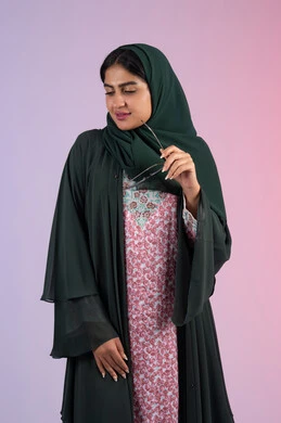 مفهوم الموضة والأناقة، عرض الأزياء والموديلات الحديثة، العناية بالجمال والإطلالة المتميزة، بورترية لسيدة عربية خليجية اماراتية مبتسمه محجبة ترتدي العباءه الملونه تمسك بيدها النظارة الشمسية ، سيدة سعودية تنظر الى الكاميرا بايماءات السعادة و السرور، خلفية ملونه