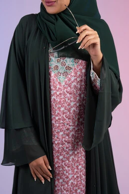 أزياء محجبات عصرية راقية، مفهوم الأناقة والاهتمام بالمظهر الخارجي، العناية بالجمال والإطلالة المتميزة، بورترية لسيدة عربية خليجية اماراتية مبتسمه محجبة ترتدي العباءه الملونه تمسك بيدها النظارة الشمسية ، سيدة سعودية تقف بايماءات الانوثه و الثقه، خلفية ملونه