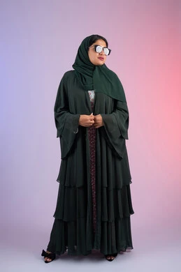 مفهوم الانوثه و الشياكة ، العناية بالجمال والإطلالة المتميزة، الأناقة والاهتمام بالمظهر الخارجي، بورترية من الجانب لسيدة عربية خليجية اماراتية مبتسمه محجبة ترتدي العباءه الملونه و النظارة الشمسية ، امراة سعودية تقف بايماءات الانوثه و الثقه، الجسم بالطول الكامل، خلفية ملونه