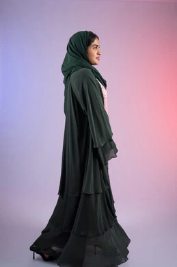 The concept of femininity and softness, beauty and interest in outward appearance, a Saudi woman looking with gestures of pleasure and happiness, a side portrait of an Arab Gulf Emirati woman wearing a hijab and an abaya, standing straight with an expression of self-confidence, full-length body, colored background