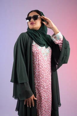 مفهوم الموضة والأناقة، إيماءات الانوثة والجمال, سيدة اماراتية ترتدي عباءة أنيقة ونظارة سوداء معاصرة، بورترية لإمرأة عربية خليجية سعودية محجبة تقوم بتجربة النظارات الشمسية الجديدة، الاهتمام بالمظهر الخارجي والاناقه ، خلفية ملونة