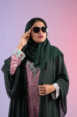 سيدة اماراتية ترتدي عباءة أنيقة ونظارة سوداء معاصرة، بورترية لإمرأة عربية خليجية سعودية محجبة تقوم بتجربة النظارات الشمسية الجديدة، الاستمتاع بإمتلاك اكسسوارات عصرية, الاهتمام بالمظهر الخارجي والاناقه ، إيماءات الانوثة والجمال, خلفية ملونة