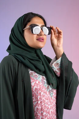 الاستمتاع بإمتلاك اكسسوارات عصرية, الاهتمام بالمظهر الخارجي والاناقه ،تعابير السرور والسعادة ، سيدة اماراتية ترتدي عباءة أنيقة ونظارة سوداء معاصرة, إيماءات الانوثة والجمال, بورترية لإمرأة عربية خليجية سعودية محجبة تقوم بتجربة النظارات الشمسية الجديدة, خلفية ملونة