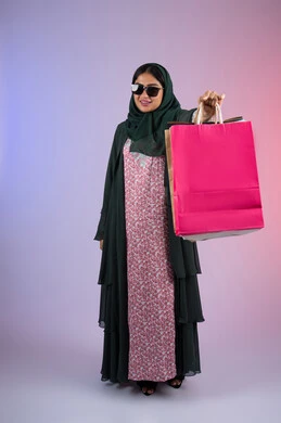 Taking advantage of offers and discounts on White Friday, the positive impact of shopping on women, an Emirati woman taking advantage of seasonal offers and discounts, a portrait of a smiling Saudi Arabian Gulf woman wearing an abaya and hijab, holding colorful shopping bags, full body, colorful background