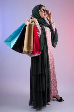 Taking advantage of offers and discounts, the positive impact of shopping on women, an Emirati woman taking advantage of seasonal offers and discounts, a side portrait of a smiling Saudi Arabian Gulf woman wearing an abaya, hijab and sunglasses, holding colorful shopping bags, full body, colorful background