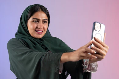 Various mobile programs and applications, use of modern technical devices, a young Saudi woman documenting happy moments, a close-up portrait of a young Arab Gulf Emirati woman holding a mobile phone in her hand, taking commemorative selfies, a colorful background Various mobile programs and applications, use of modern technical devices, a young Saudi woman documenting happy moments, a close-up portrait of a young Arab Gulf Emirati woman holding a mobile phone in her hand, taking commemorative selfies, a colorful background