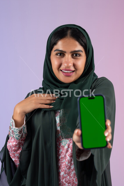 إنجاز الأعمال بسرعة وسهولة، عرض شاشة كروما خضراء فارغة على الهاتف المحمول، دمج التقنية والتكنولوجيا في الحياة العملية، بورترية لامراة عربيه خليجيه اماراتية  تحمل بيدها جوال محمول، سيده سعودية تنظر الي الكاميرا بايماءات السعادة و السرور ، خلفية ملونه