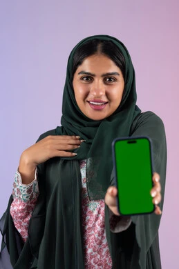 إنجاز الأعمال بسرعة وسهولة، عرض شاشة كروما خضراء فارغة على الهاتف المحمول، دمج التقنية والتكنولوجيا في الحياة العملية، بورترية لامراة عربيه خليجيه اماراتية  تحمل بيدها جوال محمول، سيده سعودية تنظر الي الكاميرا بايماءات السعادة و السرور ، خلفية ملونه