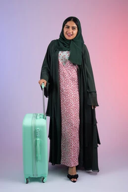 الاستعداد لموعد الرحلة, شابة سعودية تستعد لقضاء رحلة صيفية ممتعة, بورتريه لشابة عربية خليجية عمانية محجبة ترتدي العباءة الملونه  تمسك حقيبة السفر,ايماءات السعادة و السرور، صورة الجسم بالطول الكامل, خلفية ملونه