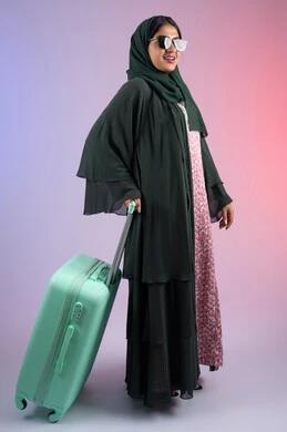 قضاء أوقات ممتعة ومسلية في الإجازة، الشعور بالسعادة والفرح, شابة سعودية تستعد لقضاء رحلة صيفية ممتعة, بورتريه لشابة عربية خليجية عمانية محجبة ترتدي العباءة الملونه و النظارة الشمسية  تمسك حقيبة السفر بإيماءات الحماس, صورة الجسم بالطول الكامل, خلفية ملونه