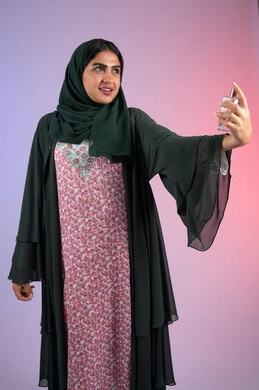 التطيب بالروائح الفريدة, التسويق لمنتجات العطور ، سيدة اماراتية تستخدم المستحضرات النسائية, بورترية لامرأة عربيه سعودية خليجية محجبة مبتسمة تمسك بيدها زجاجة وتقوم برش العطر، خلفية ملونة