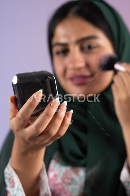 The concept of femininity and interest in external appearance, makeup and makeup tutorial, marketing of beauty products, close-up portrait of a Saudi Arabian Gulf girl wearing an abaya and hijab holding a blush brush, an Emirati woman using modern women's cosmetics, a high-end women's salon, a colorful background