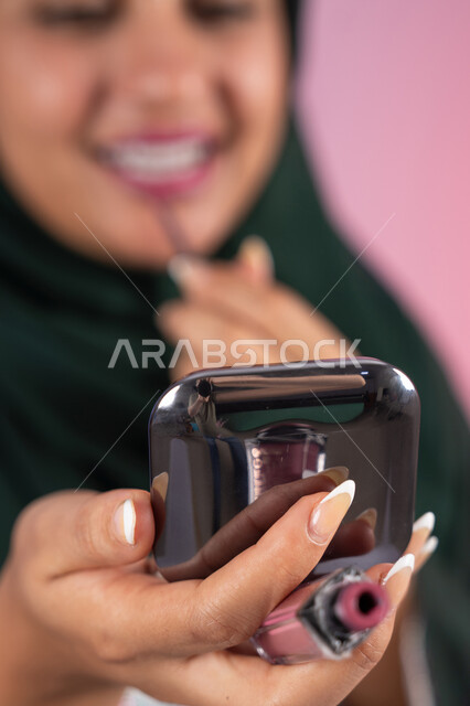 التسويق لمنتجات التجميل، مفهوم الانوثه والاهتمام بالمظهر الخارجي، مكياج وميكاب تتوريال، سيدة اماراتية تستخدم أدوات تجميل نسائيه عصريه، بورترية مقرب ليد فتاه عربيه سعودية خليجيه ترتدي العباءة والحجاب تقوم بوضع احمر الشفاة ، خلفية ملونه