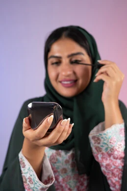 International women's products, the concept of elegance and interest in external appearance, drawing eyes using mascara, a close-up portrait of a veiled Saudi Arabian Gulf woman enjoying women's decoration, an Emirati woman wearing an elegant abaya and using cosmetics, a colorful background