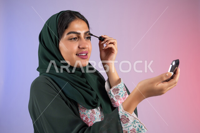 Drawing eyes using mascara, international women's products, the concept of elegance and interest in external appearance, a close-up portrait of a veiled Saudi Arabian Gulf woman enjoying women's decoration, an Emirati woman wearing an elegant abaya and using cosmetics, a colorful background