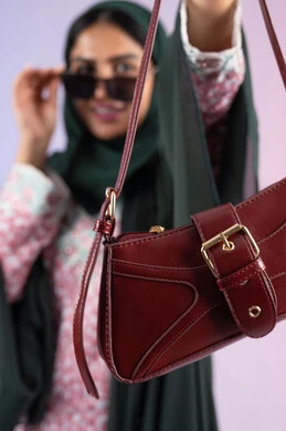 التسويق للمنتجات الاماراتية والماركات العالمية، عرض الأزياء والحقائب والاكسسوارات بالتصاميم الحديثة, متابعة صيحات الموضة، بورتريه مقرب لامراة عربية خليجية اماراتية مبتسمة ترتدي نظارات شمسية عصرية، سيده سعودية تحمل بيدها حقيبة فاخرة, خلفية ملونة