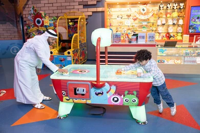 طفل خليجي يرتدي الزي الكاجوال يستمتع بلعبة الهوكي الهوائي، رجل عربي خليجي اماراتي يرتدي الكندورة و الغترة يشارك ابنه في اللعب، الأنشطة الترفيهيه الممتعة، ايماءات الاندماج والتفاعل ، قضاء الاوقات السعيدة مع العائلة، منافسة مليئة بالتحدي والإثارة