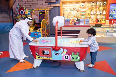An Emirati Gulf Arab man wearing a kandura and ghutra participating with his son in playing, fun recreational activities, gestures of integration and interaction, spending happy times with the family, a competition full of challenge and excitement, a Gulf child wearing casual clothes enjoying a game of air hockey An Emirati Gulf Arab man wearing a kandura and ghutra participating with his son in playing, fun recreational activities, gestures of integration and interaction, spending happy times with the family, a competition full of challenge and excitement, a Gulf child wearing casual clothes enjoying a game of air hockey