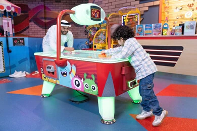 ايماءات الاندماج والتفاعل ، قضاء الاوقات السعيدة مع العائلة، الأنشطة الترفيهيه الممتعة ، منافسة مليئة بالتحدي والإثارة ،رجل عربي خليجي اماراتي يرتدي الكندورة و الغترة يشارك ابنه في اللعب، طفل خليجي يرتدي الزي الكاجوال يستمتع بلعبة الهوكي الهوائي