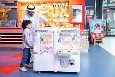 ايماءات الاندماج والتفاعل، تعابير السرور والسعادة، أجواء تفاعلية مبهجة ، انشطة صيفية ترفيهية، رجل عربي خليجي اماراتي يرتدي الكندورة و الغترة يشارك ابنه في اللعب، لحظات المرح والحماس، طفل خليجي يرتدي الزي الكاجوال يقوم  بلعب على اله المخلب