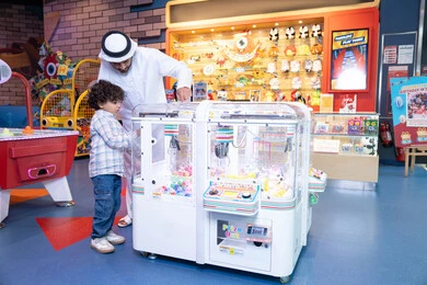 ايماءات الاندماج والتفاعل، عطلة صيفية سعيدة، رجل عربي خليجي اماراتي يرتدي الكندورة و الغترة يشارك ابنه في اللعب، أجواء تفاعلية مبهجة ، مشاركة الأب ابنه لحظات المرح والحماس ، تعابير السرور والسعادة، طفل خليجي يرتدي الزي الكاجوال يقوم  بلعب على اله المخلب