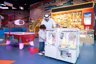 قضاء الاوقات السعيدة، رجل عربي خليجي اماراتي يرتدي الكندورة و الغتره يستمتع بقضاء وقت العطله مع ابنه، أجواء تفاعلية مبهجة ، مشاركة الأب ابنه لحظات المرح والحماس ، تعابير السرور والسعادة، طفل خليجي يرتدي الزي الكاجوال يقوم  بلعب على اله المخلب