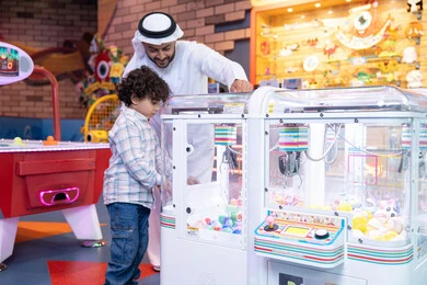 Advanced gaming halls, an Emirati Gulf Arab man wearing a kandura and ghutra enjoying his vacation time with his son, a cheerful interactive atmosphere, the father sharing moments of fun and excitement with his son, expressions of pleasure and happiness, a Gulf child wearing casual clothes playing on the claw machine Advanced gaming halls, an Emirati Gulf Arab man wearing a kandura and ghutra enjoying his vacation time with his son, a cheerful interactive atmosphere, the father sharing moments of fun and excitement with his son, expressions of pleasure and happiness, a Gulf child wearing casual clothes playing on the claw machine