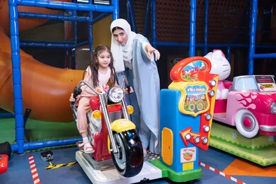 مركز ألعاب ترفيهي، ام عربيه خليجيه اماراتية ترتدي العباءه الملونه تقوم بقضاء وقت ممتع مع طفلتها فى مدينة الالعاب، العاب الكترونية ، التسلية و الترفيه ، طفلة خليجيه ترتدي الزي الكاجوال تركب لعبة الدراجة بايماءات السعادة و السرور