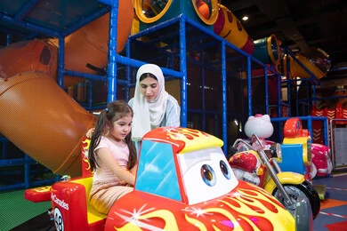 الاستمتاع بقضاء أوقات مسلية ايام العطلة، ام عربيه خليجيه اماراتية ترتدي العباءه الملونه تقوم بقضاء وقت ممتع مع طفلتها فى مدينة الالعاب، العاب الكترونية ، التسلية و الترفيه ، طفلة خليجيه ترتدي الزي الكاجوال تركب لعبة الدراجة بايماءات السعادة و السرور