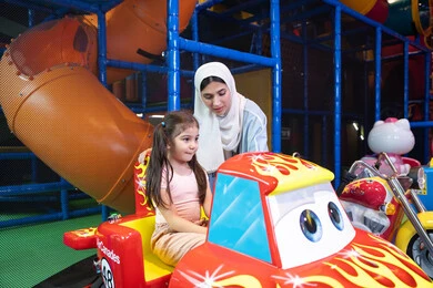 Fun recreational activities, an Emirati Gulf Arab mother wearing a colorful abaya spending a fun time with her daughter in an amusement park, electronic games, entertainment and recreation, a Gulf girl wearing casual clothes riding a bicycle with gestures of happiness and pleasure