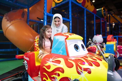 ام عربيه خليجيه اماراتية ترتدي العباءه الملونه تقوم بقضاء وقت ممتع مع طفلتها فى مدينة الالعاب، العاب الكترونية ، التسلية و الترفيه ، الترفيه في العطلة الصيفية، طفلة خليجيه ترتدي الزي الكاجوال تركب لعبة الدراجة بايماءات السعادة و السرور