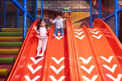 Children participating in recreational activities, sliding on the slide, gestures of joy and happiness, two Emirati Gulf Arab children wearing casual clothes enjoying playing on the slide, exploiting free time in entertainment and play