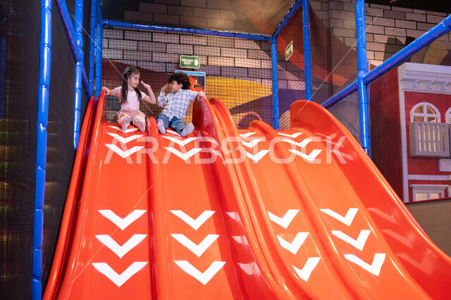 اصطحاب الأطفال إلى الصالة المخصصة للعب، التزحلق على الزحليقه, ايماءات المرح و السرور, طفلان عربيان خليجيان اماراتيان يرتديان الزي الكاجوال يستمتعان باللعب على لعبة التزحلق، استغلال وقت الفراغ في التسلية واللعب ,قضاء أوقات ممتعة في المدينة الترفيهيه