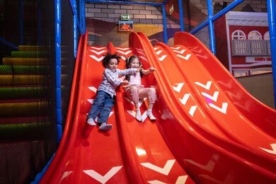 Gestures of fun and happiness, skating on the slide, two Emirati Gulf Arab children wearing casual clothes enjoying playing on the slide, exploiting free time in entertainment and playing, enjoying playing on a sunny day, spending fun times in the entertainment city