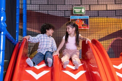 التزحلق على الزحليقه, ايماءات المرح و السرور, طفلان عربيان خليجيان اماراتيان يرتديان الزي الكاجوال يستمتعان باللعب على لعبة التزحلق، استغلال وقت الفراغ في التسلية واللعب, الإستمتاع باللعب في يوم مشمس, ,قضاء أوقات ممتعة في المدينة الترفيهيه