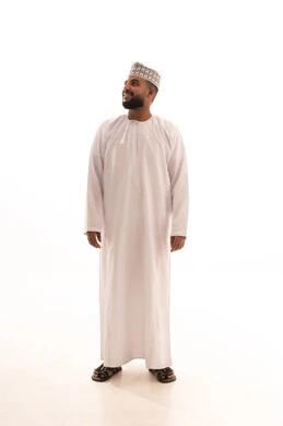 Standing upright and looking with gestures of self-confidence, gazing at something, paying attention to external appearance, the concept of elegance and masculinity, a portrait of a young Arab Gulf Omani man wearing a dishdasha and kumma with expressions of cheerfulness and joy, full body length, white background.