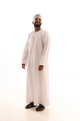 Looking at something, paying attention to the external appearance, standing upright and looking with gestures of self-confidence, the concept of elegance and masculinity, a portrait of a young Arab Gulf Omani man wearing a dishdasha and kumma with expressions of cheerfulness and joy, full body length, white background.