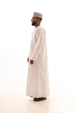 الاهتمام بالمظهر الخارجي، الوقوف باستقامة والنظر بايماءات الثقة بالنفس, مفهوم الاناقة والرجولة, بورتريه من الجانب لشاب عربي خليجي عماني يرتدي الدشداشة والكمه بتعابير البشاشة والسرور, الطول الكامل للجسم، خلفية بيضاء