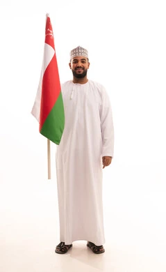 تعابير السعادة و السرور، مفهوم حب الوطن والإنتماء إليه، الاعتزاز والفخر بالرموز والراية العمانية، المشاركة بالاعياد والمناسبات الوطنية، الاحتفال بذكرى اليوم الوطني العماني، بورتريه لشاب عربي خليجي عماني يرتدي الدشداشة والكمه يمسك بيدية علم عمان، الجسم بالطول الكامل، خلفية بيضاء